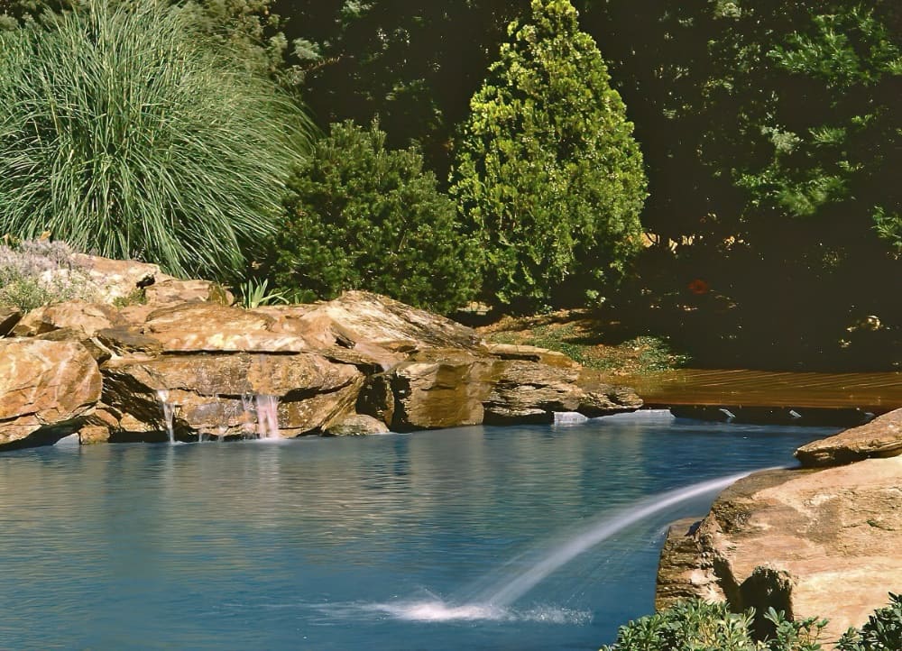 Landscaped infinity pool surrounded by natural rocks and lush greenery, with water jets and a small waterfall