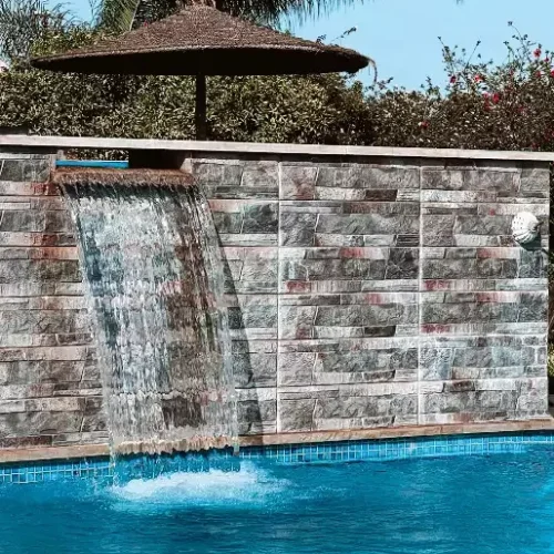 Modern blade waterfall feature cascading into a luxury outdoor pool, set against a stone-clad wall.