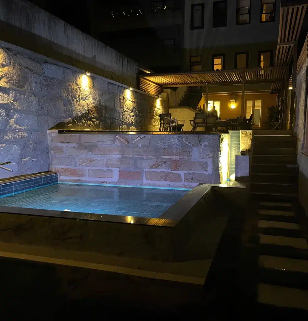 Night view of the Porto infinity pool with soft lighting on the balancing tank and natural stone walls