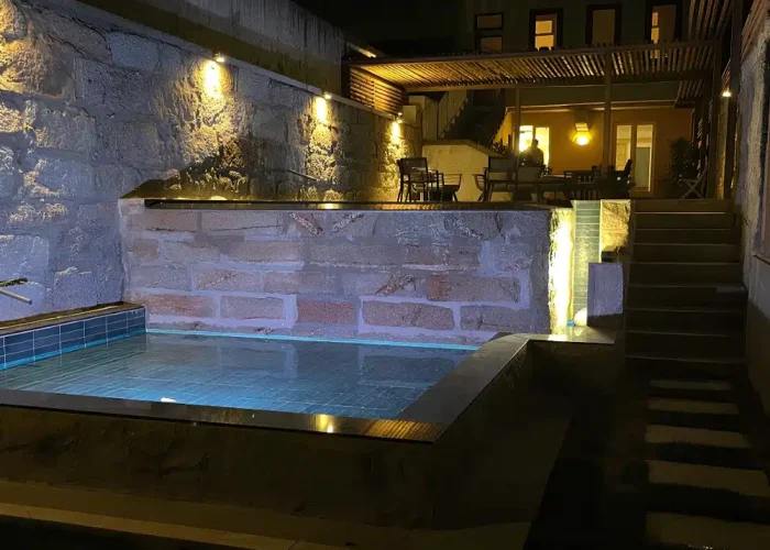 Night view of the Porto infinity pool with soft lighting on the balancing tank and natural stone walls